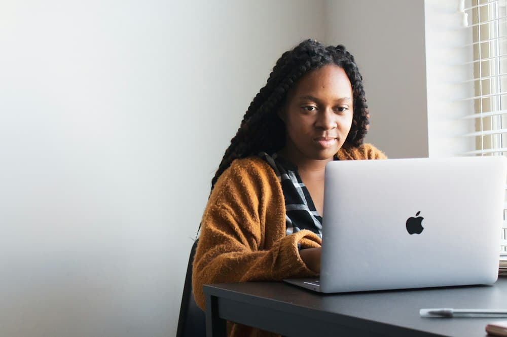 A woman with long braids working on a laptop at her desk
